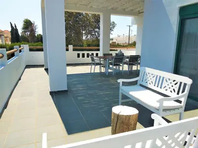 a porch with a white bench and tables and chairs at Villa Akti in Lachania
