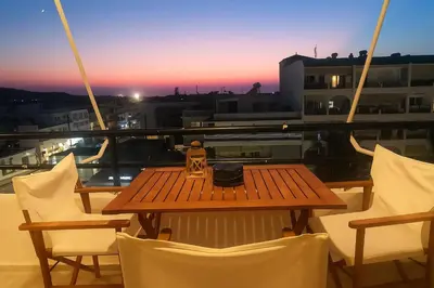 a table and chairs on a balcony with a sunset at Apartment Dream Holidays - 500 meters to beach in Ialyssos
