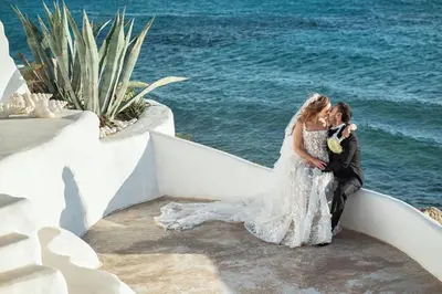 a bride and groom sitting on a ledge near the water at Axiotheaton Villas in Pefki Rhodes