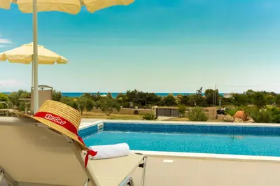 a straw hat sitting on a chair next to a swimming pool at Orianna Sea View Villa in Gennadi