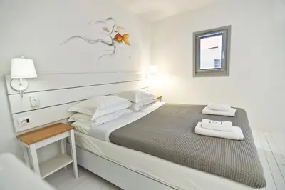 a white bedroom with a large bed and a window at Lindos Comfy Suites in Líndos