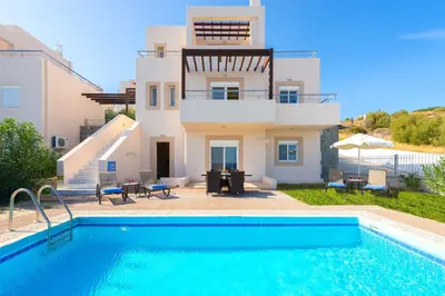 a villa with a swimming pool in front of a house at Athoniki Villas in Kalathos