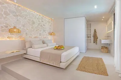 a bedroom with a white bed and a stone wall at Milos Villas Complex in Pefki Rhodes