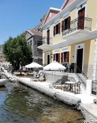 a building with tables and umbrellas next to a river at Perla di Mare in Symi