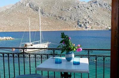 a table on a balcony with a boat in the water at Perla di Mare in Symi