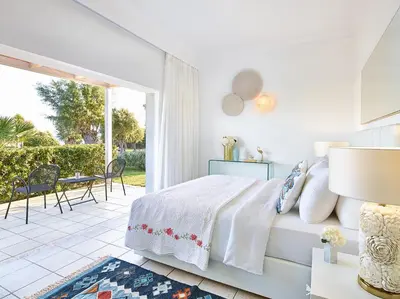 a white bedroom with a bed and a patio at Grecotel LUXME Dama Dama in Faliraki