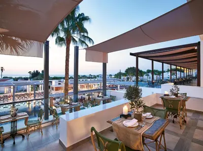 a restaurant with tables and chairs and a view of a pool at Grecotel LUXME Dama Dama in Faliraki
