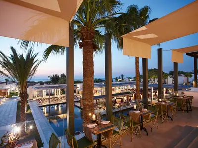 a restaurant with tables and palm trees and a pool at Grecotel LUXME Dama Dama in Faliraki