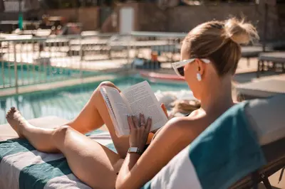 a woman sitting next to a swimming pool reading a book at Lambis Studios & Apartments in Líndos
