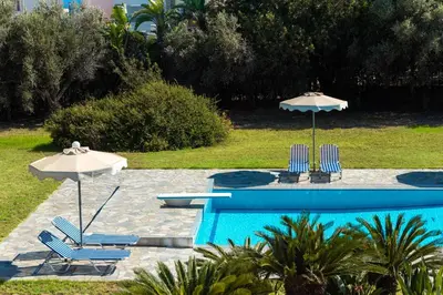 a swimming pool with two chairs and two umbrellas at Sutherlea in Koskinou