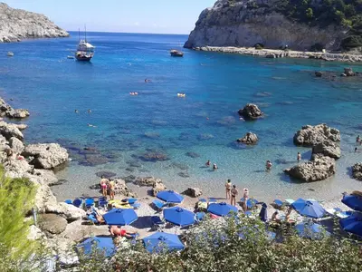 a beach with blue umbrellas and people in the water at COLONIAL FAMILY apartment #3 in Faliraki