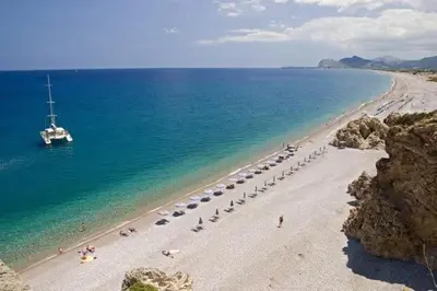 a beach with umbrellas and a boat in the water at COLONIAL FAMILY apartment #3 in Faliraki