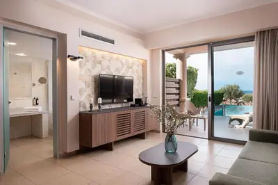 a living room with a television and a living room with a couch at KRESTEN ROYAL Euphoria Resort in Kallithea Rhodes