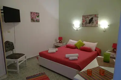 a bedroom with a bed with red sheets and green pillows at Green Garden Studios in Koskinou