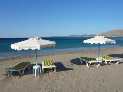 three lounge chairs and umbrellas on a beach at Villa Lia Panorama in Pefki Rhodes
