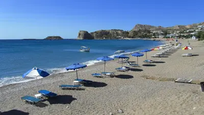 a beach with chairs and umbrellas and a row of chairs and tables at Kaya Sea Studios - Stegna Beach in Archangelos
