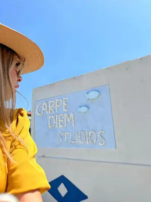 a woman wearing a hat sitting in front of a sign at Carpe Diem Studios in Ialyssos