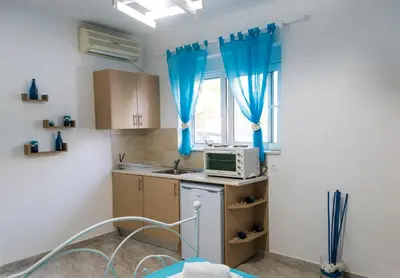 a kitchen with a microwave and a window with blue curtains at Carpe Diem Studios in Ialyssos