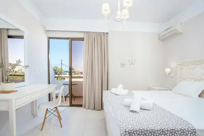 a white bedroom with two beds and a desk at Voula Studios in Faliraki