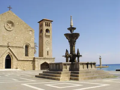 a church with a clock tower and a fountain at Ixia Beach in Ialyssos