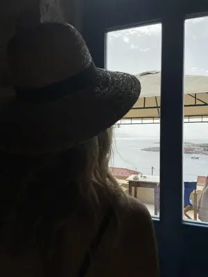 a person wearing a hat looking out a window at Marina Castellana Studios in Halki