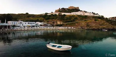 a small boat in the water in front of a town at Villa Eftihia in Lindos in Líndos