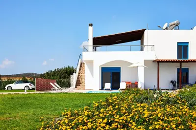 a white house with yellow flowers in the yard at Nerida Beachfront Villas in Plimmiri
