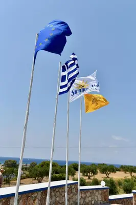 three flags on poles in front of a wall at Summer View in Theologos