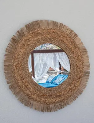 a round rattan mirror hanging on a wall at Maripaul Family Villa in Lardos