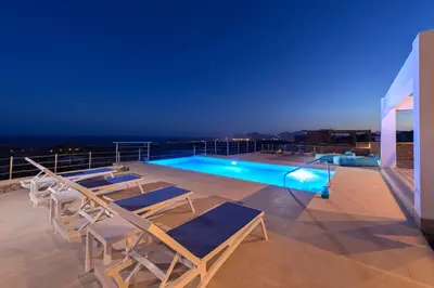 a deck with chairs and a swimming pool at night at Villa Olympos in Afantou
