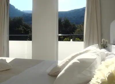 a white bedroom with a view of a mountain at Blugreen Stegna Suites and Apartments in Archangelos