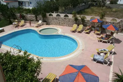 a pool with chairs and umbrellas and people sitting around it at Sevastos Studios in Faliraki