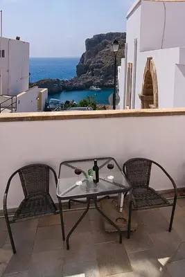 a table with two chairs and a bottle of wine on a balcony at Lindos Panorama in Líndos