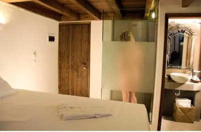a woman standing in a bathroom with a bed and a sink at Domus Studios in Rhodes Town