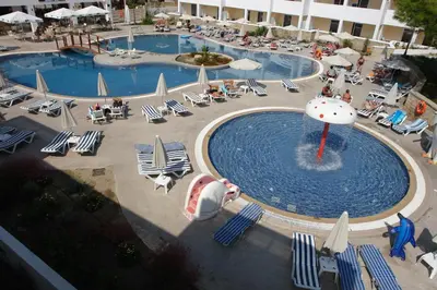 a pool with chairs and umbrellas and people sitting around it at Matina Pefkos Aparthotel in Pefki Rhodes