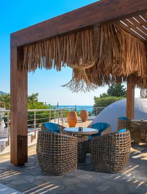 a patio with a table and chairs under a straw umbrella at Porto Angeli in Archangelos
