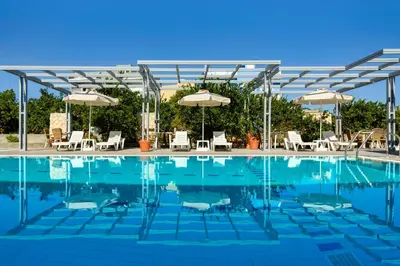 a swimming pool with chairs and umbrellas at Ilyssion Holidays Hotel in Ialyssos