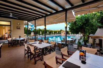 a restaurant with tables and chairs and a swimming pool at Ilyssion Holidays Hotel in Ialyssos
