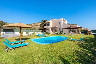 a pool with chairs and an umbrella and a house at Aelia Luxury Apartment-with swimming pool in Afantou