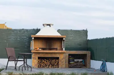 a outdoor grill with a table and chairs in front of a wall at Aelia Luxury Apartment-with swimming pool in Afantou