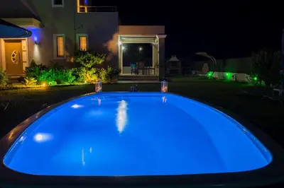 a large blue swimming pool in a yard at night at Aelia Luxury Apartment-with swimming pool in Afantou