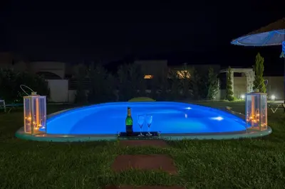 a swimming pool at night with a bottle of wine and glasses at Aelia Luxury Apartment-with swimming pool in Afantou