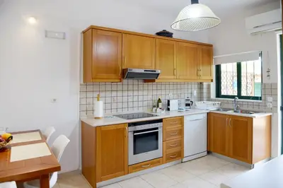 a kitchen with wooden cabinets and white appliances at Athina's Apartment in Olive Grove in Faliraki