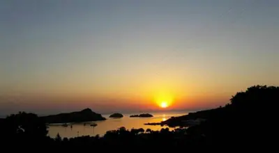 a sunset over a body of water with the sun setting at Aphrodite White Studios Lindos in Líndos
