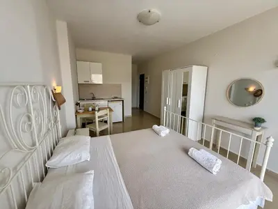 a bedroom with a white bed and a kitchen at Steve's Beach in Faliraki