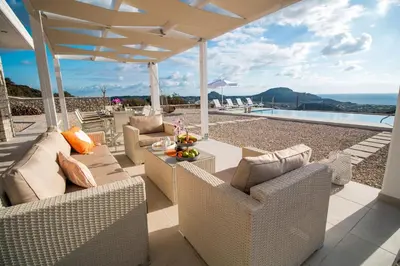 a patio with chairs and a table with a view of the ocean at Francis & Gregorys Luxury Villas in Afantou