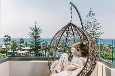 a woman sitting in a hammock on a balcony overlooking the ocean at Sheraton Rhodes Resort in Ixia