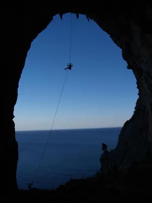 a person on a rope in a cave with the ocean at The Grandma House in Ialyssos