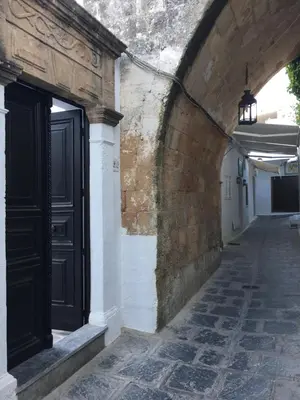 an alley with a black door and a brick wall at Lindos Tholos Villa in Líndos