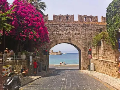 an old stone archway with pink flowers next to the ocean at Praxitelous 9 Old Town in Rhodes Town